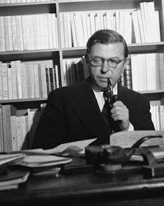 Black and white photo of a man in a study with pipe.