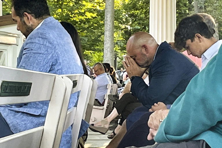 Several people sitting in a rows with heads bowed.