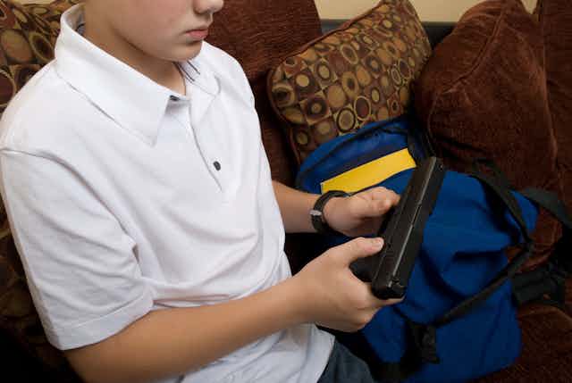 A boy in a white shirt inspects a gun he holds in his hands.
