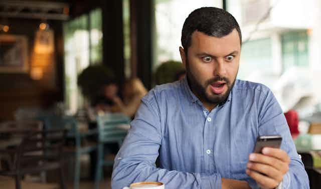 A man is seen gasping in shock at his phone.