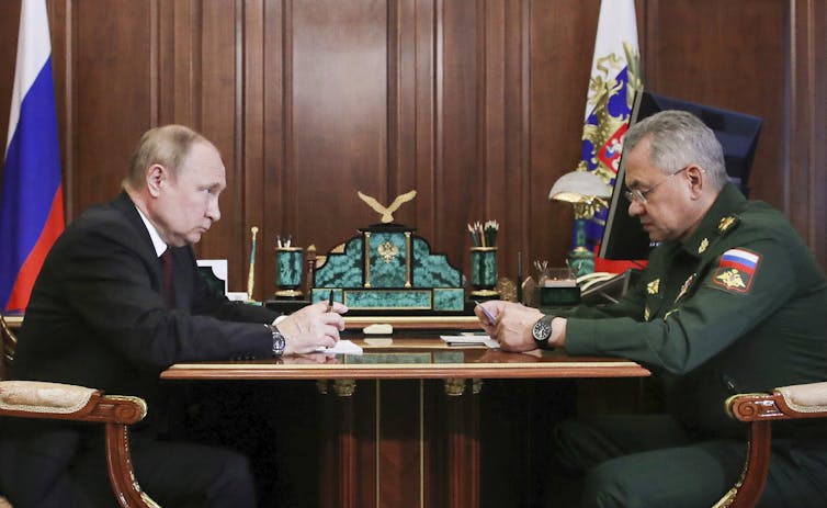 Two men, one in a suit, the other in a uniform, talking across a table.