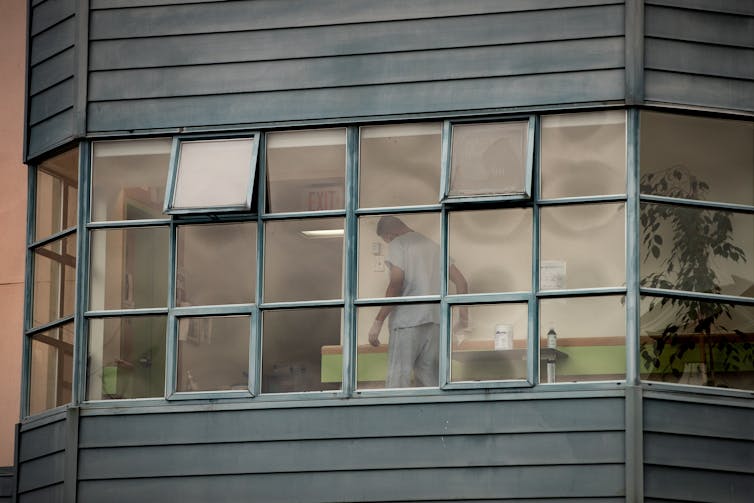 A person stands behind square windows, wearing scrubs, wiping down a desk
