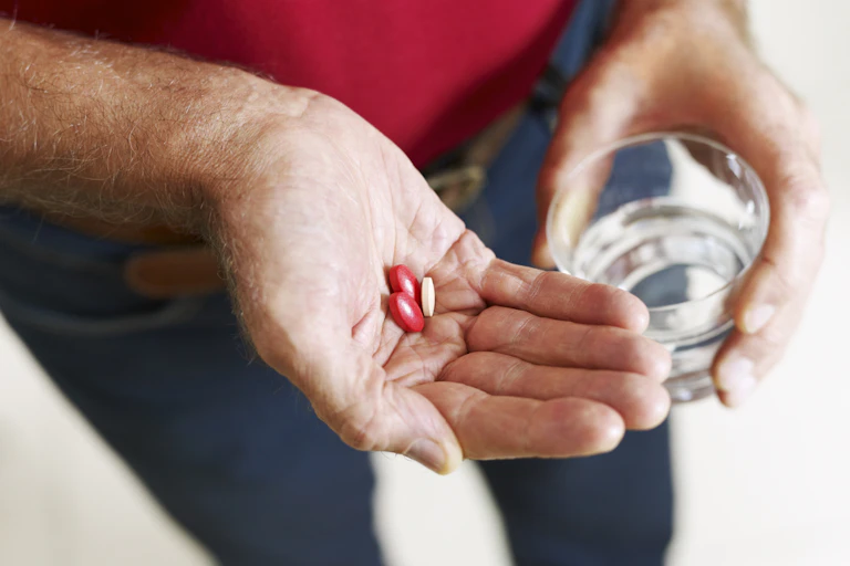 Person standing holding pills in one hand, glass of water in other