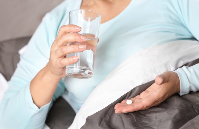 Woman lying on side in bed holding glass of water and a pill
