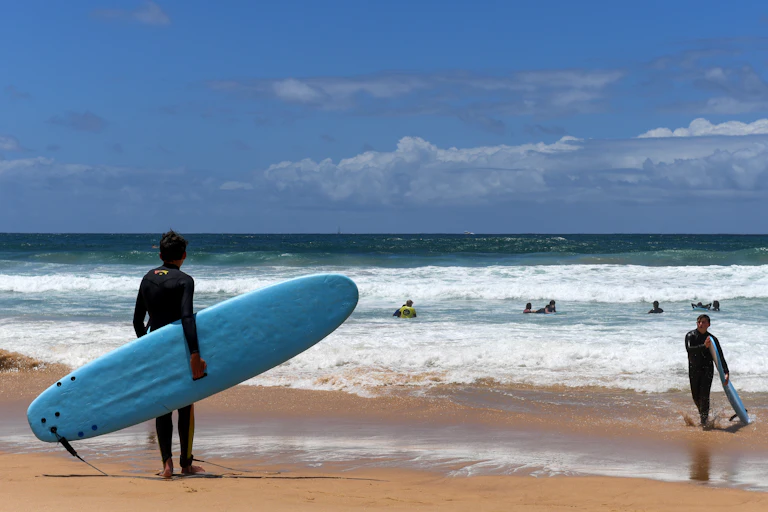surfer holds board in from of ocean and swimmers