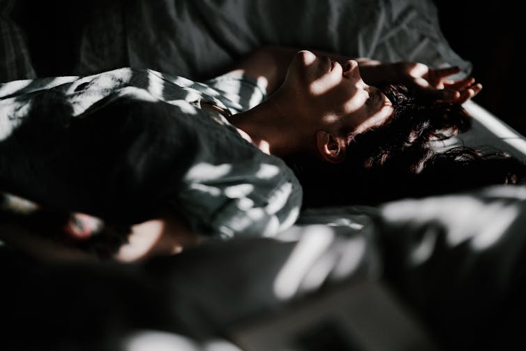 Woman lays in bed, with sun coming through blinds