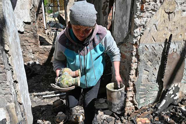 Una mujer saca dos pequeños jarrones de las ruinas de un edificio