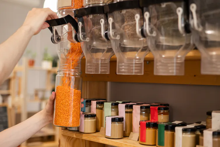 A person fills a mason jar with red lentils.
