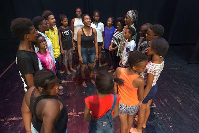 A group of young Black actors rehearsing a play in a circle.