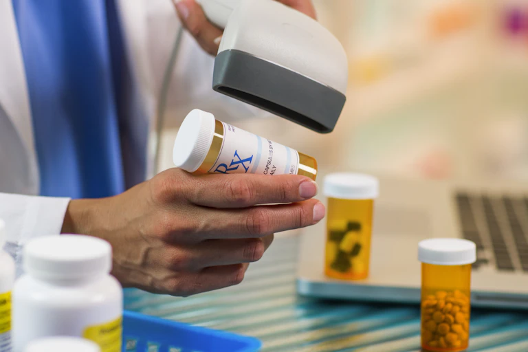 Close up of the hands of a pharmacist in a lab coat scanning bottles of pills.