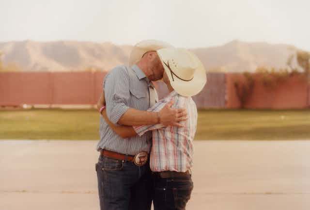 Two men in cowboy hats kissing.