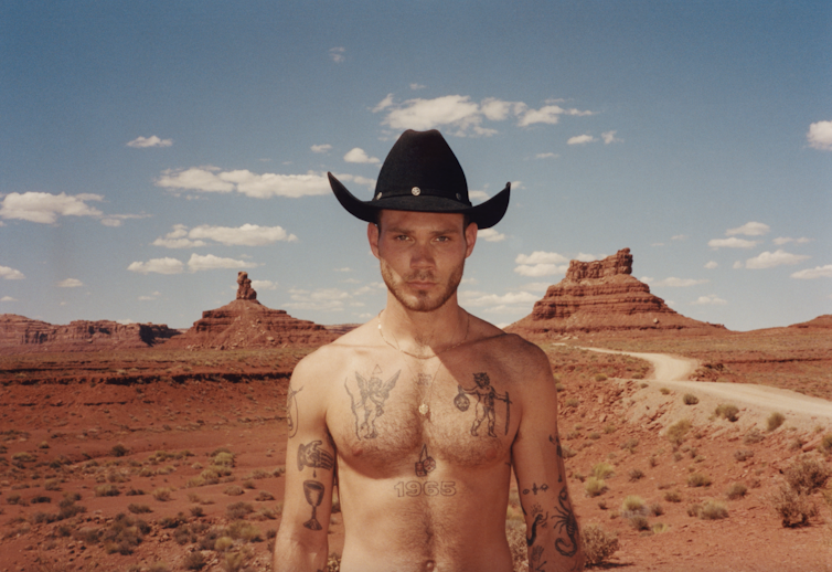 Shirtless man with tattoos and a cowboy hat.