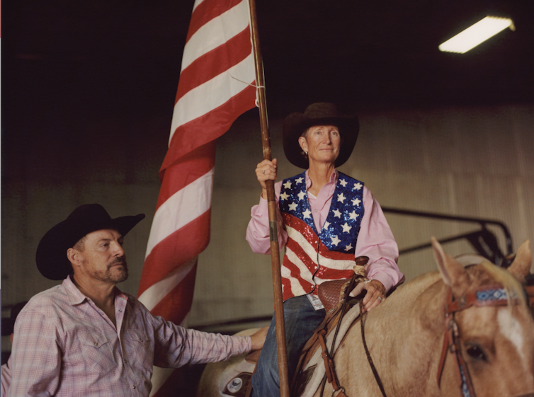 Woman on horseback wears a stars and stripes vest and holds an American flag.