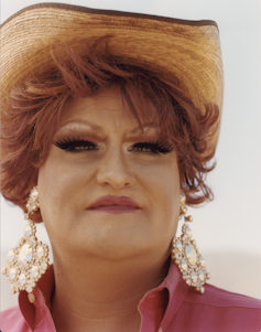 Portrait of woman wearing earrings, a pink shirt and a cowboy hat.