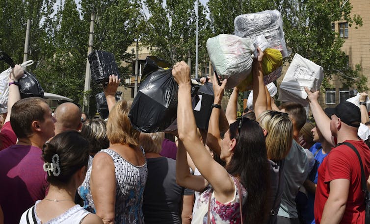 People hold packages above their heads in a crowd.