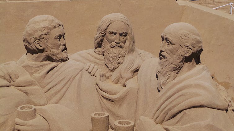 Greco-Roman style sand sculpture of three bearded men wearing robes