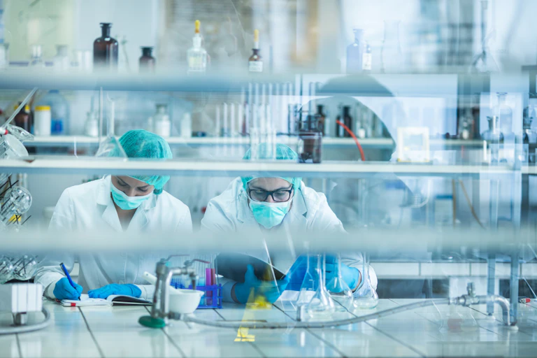 View through a glass of two forensic scientists analyzing medical data in a laboratory.