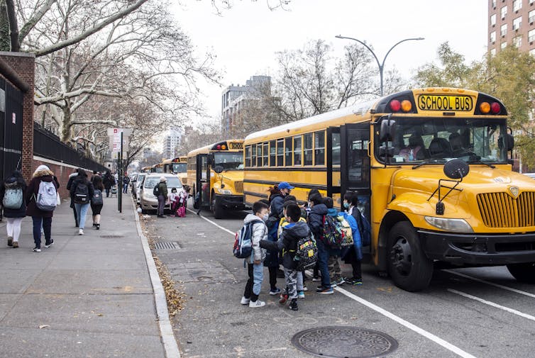 Students standing and waiting for a bus outside.