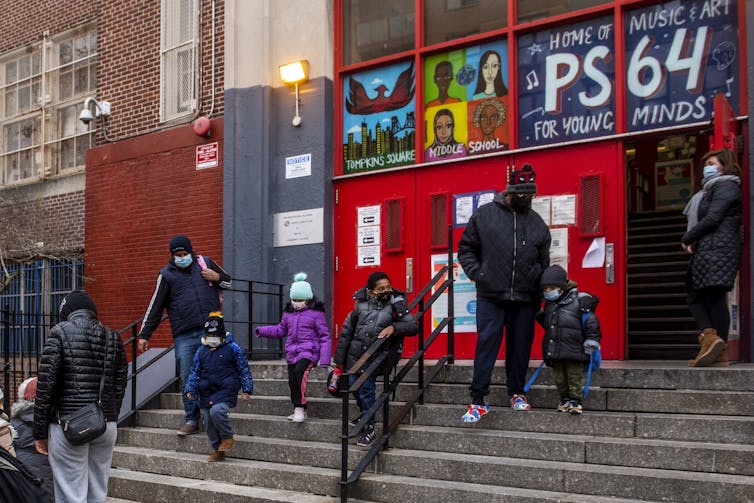 Caregivers and children seen descending the steps of a school.