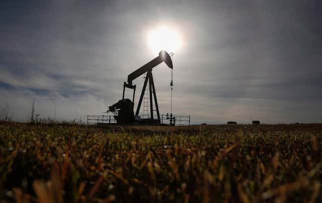 A pumpjack works at a well head in an empty field