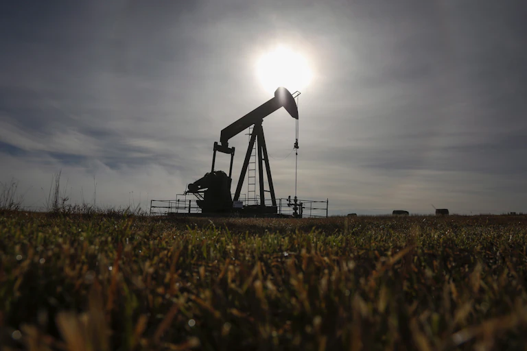 A pumpjack works at a well head in an empty field