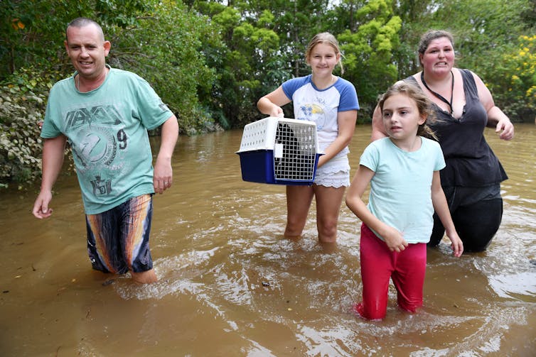 family walks through floodwaters, including girl holding pet carrier