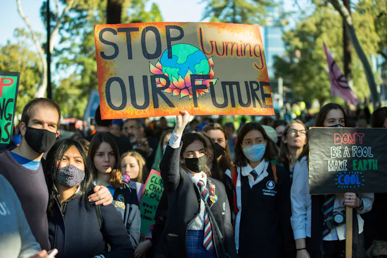 Protestors holding signs and banners and wearing covid-19 masks and school uniforms.