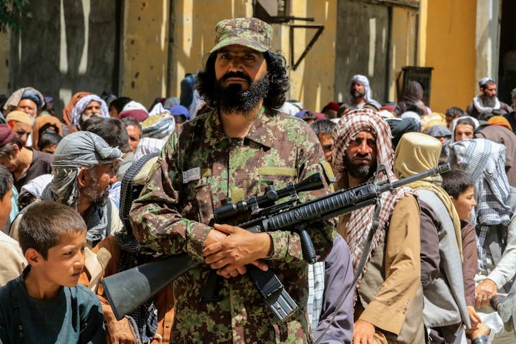 Armed guard stands in front of crowd of Afghan citizens.