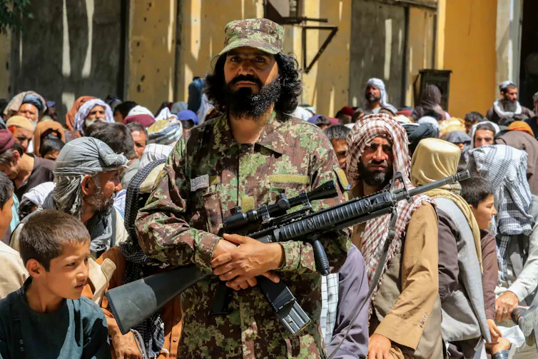 Armed guard stands in front of crowd of Afghan citizens.