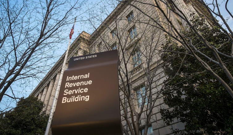 A sign reads Internal Revenue Service in front of a large stone building