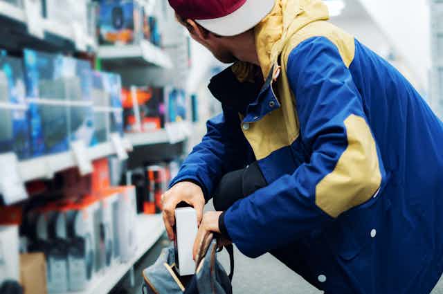 Un hombre en una tienda de electrónica se pone en cuclillas y coloca discretamente una caja en su mochila.