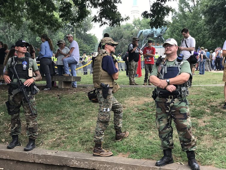 Tres hombres vestidos de militares portan armas en una manifestación.