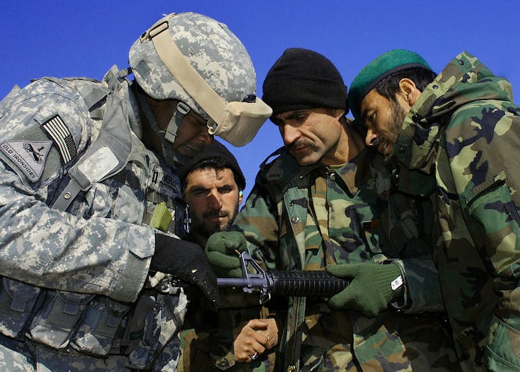 Un militar estadounidense enseña a un militar afgano cómo operar un rifle.