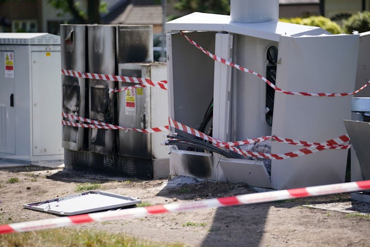 Caution tape wrapped around burned out metal boxes.