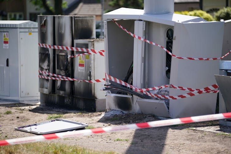 Caution tape wrapped around burned out metal boxes.