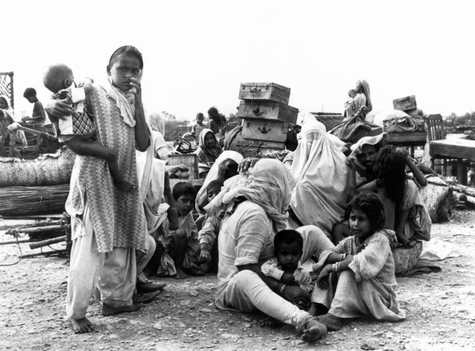 A black and white photograph of a family in Pakistan sitting on the ground among suitcases.
