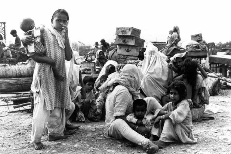 A black and white photograph of a family in Pakistan sitting on the ground among suitcases.