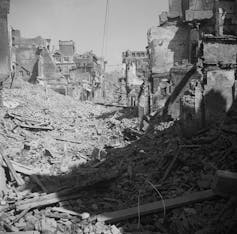 A black and white photograph shows a street of buildings turned to rubble.