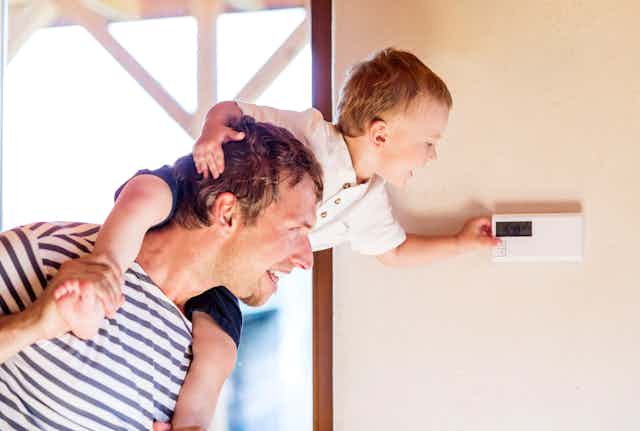 toddler sitting on man's shoulders pushes button on thermostat