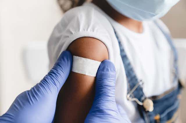 Health worker putting Bandaid on upper arm of child wearing mask 