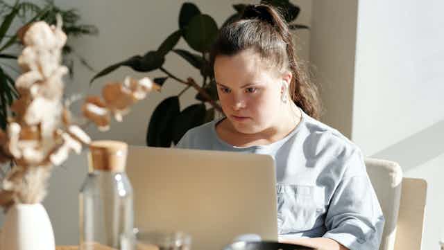 young woman with downs syndrome sits at laptop