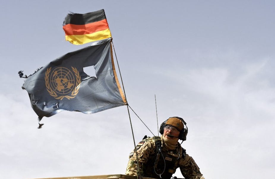 Un soldat parachutiste allemand porte les drapeaux de l'Allemagne et des Nations Unies