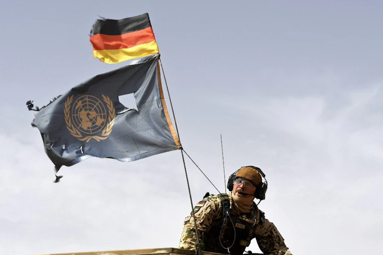 Un soldat parachutiste allemand porte les drapeaux de l'Allemagne et des Nations Unies