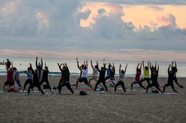 A group of people participate in a yoga session taught on the beach at sunrise.