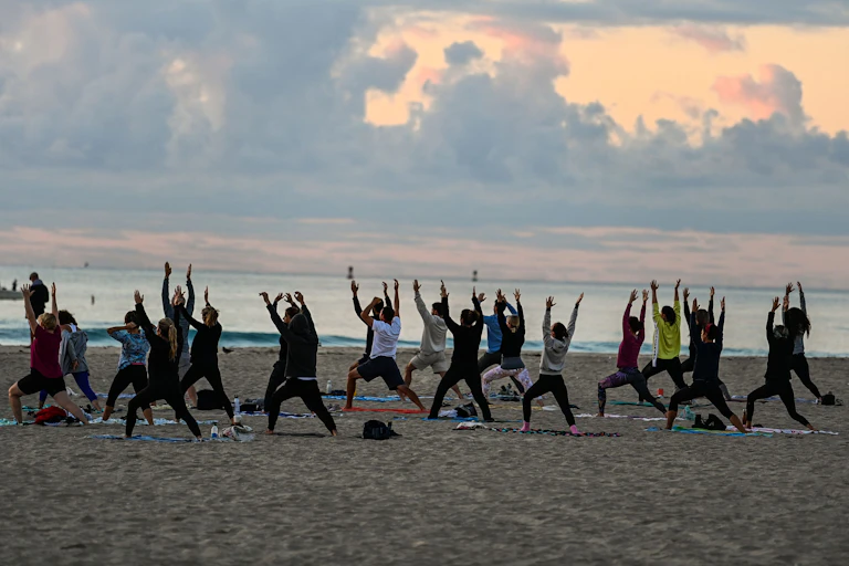 A group of people participate in a yoga session taught on the beach at sunrise.