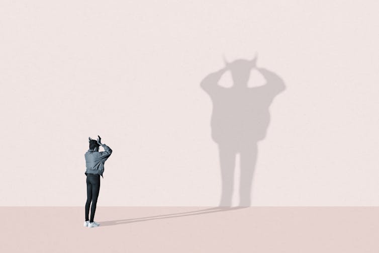 shadow with devil horns against pink background projected past a person
