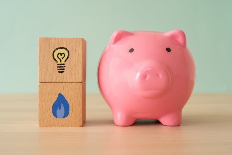 A piggy bank next to a wooden block with a picture of lightbulb and a gas flame on it.