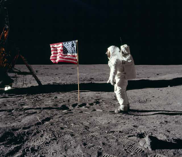 A person in a spacesuit saluting the U.S. flag on the surface of the Moon.
