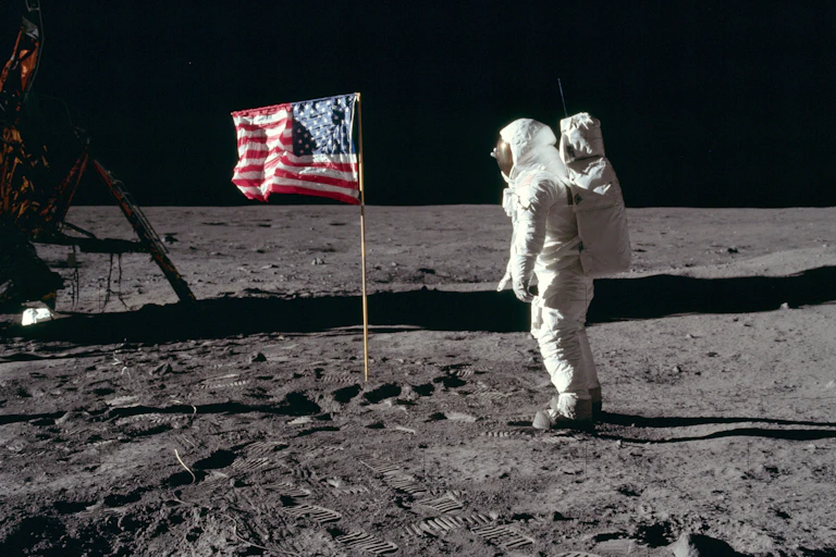 A person in a spacesuit saluting the U.S. flag on the surface of the Moon.