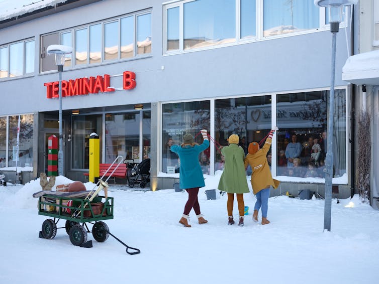 Three people in the snow; a crowd watches through windows.